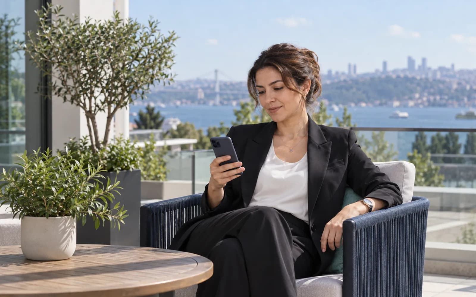 Güneşli bir terasta telefonuna bakan, rahat bir klinik yöneticisi (ekran okunmaz).