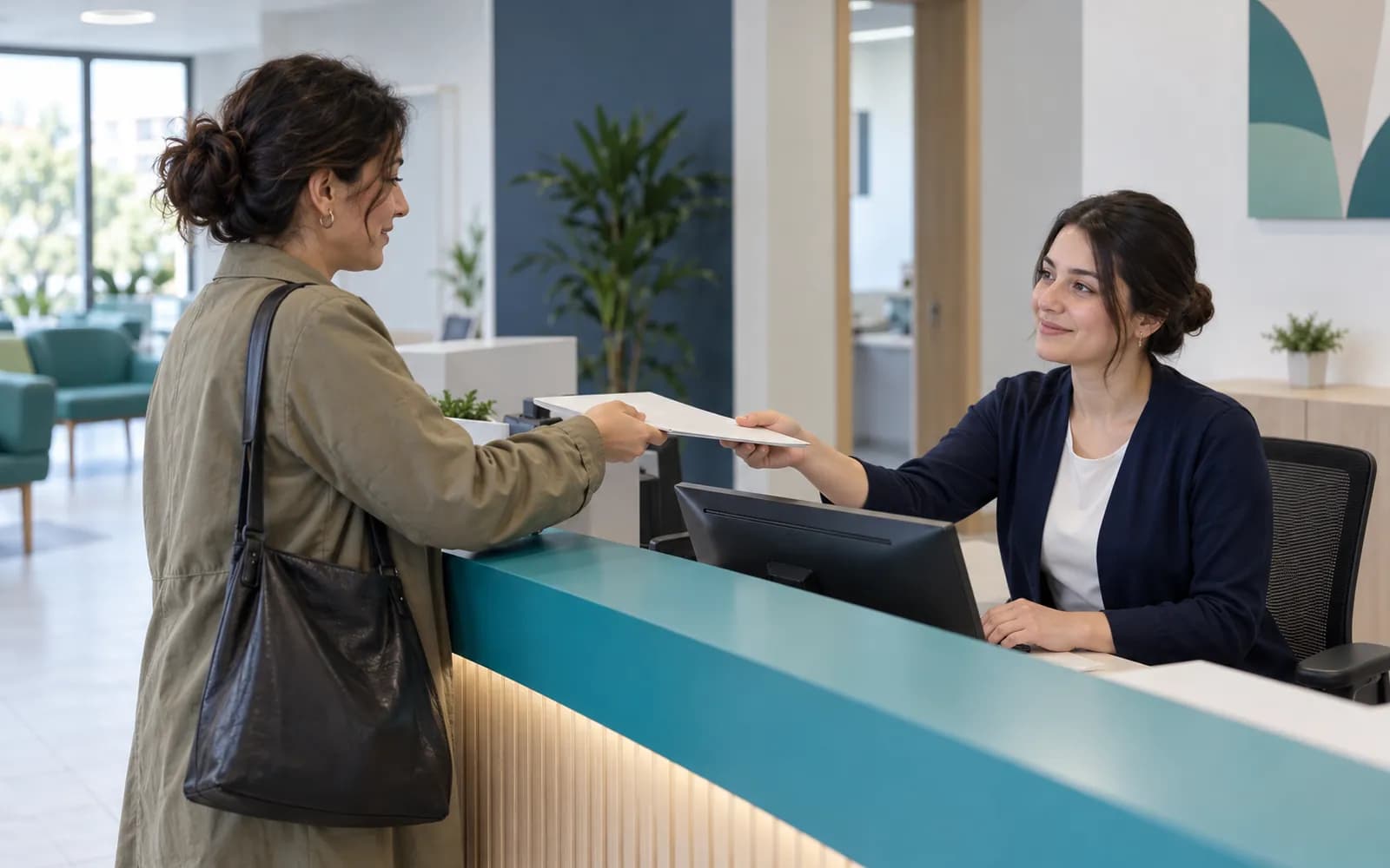 Yeni hastayı kaydeden ön büro görevlisi ve tezgahtan kapalı belge uzatan hasta
